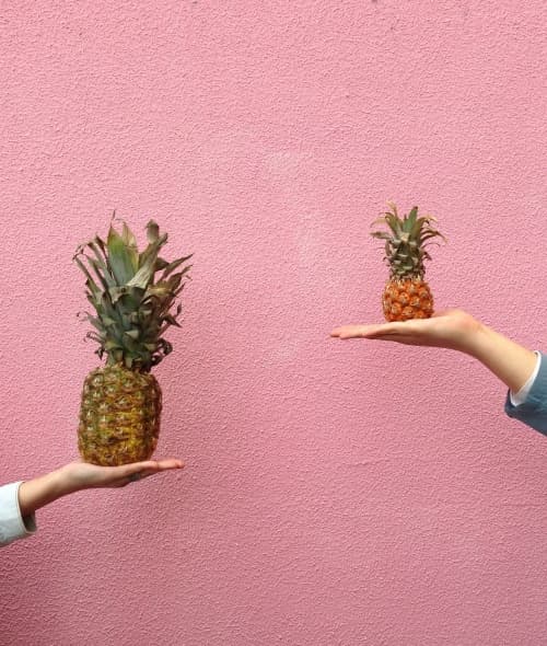 Two hands holding a small and a big pineapple